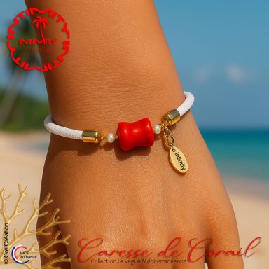 Caresse de Corail Bracelet blanc avec perles dorées et rouge, charm en forme de coquillage, sur une plage.